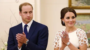 A man and woman in formal attire clap while looking to the side in an elegant room.