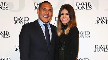 Man in a suit and woman in a black dress posing at a David Jones event backdrop.