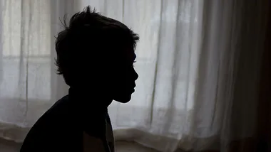Silhouette of a young child against a light curtain backdrop.