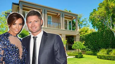 A couple stands in front of a modern house with a lush garden under a clear blue sky.