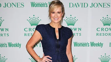 Woman in a navy dress poses at an event with logos in the background.