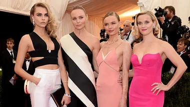 Four women in elegant gowns pose at the 2014 Met Gala, surrounded by photographers and an ornate tent.