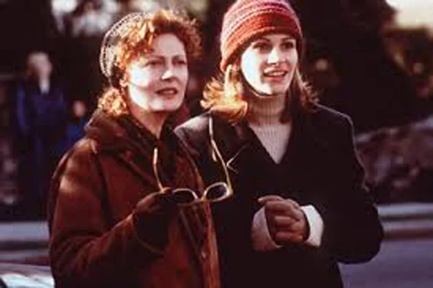 Two women standing outdoors, wearing winter clothing and hats, one holding glasses.