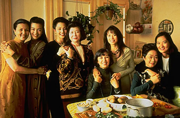 Group of women standing in a cozy kitchen, smiling and embracing, with a table set for cooking in the foreground.