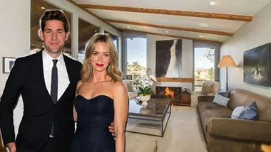 A couple poses in a stylish living room with modern decor, wooden beams, a fireplace, and large windows.