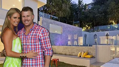Couple embracing in front of a modern, illuminated home with a garden and outdoor seating at night.