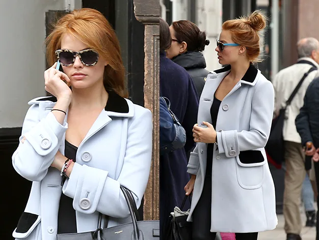 Red-haired woman in glasses and a light coat, talking on the phone and walking on a busy street.