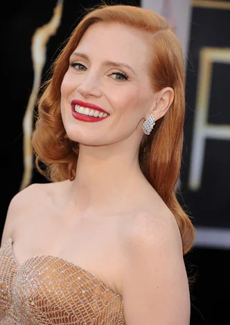 Red-haired woman in an elegant strapless gown smiling at an event.