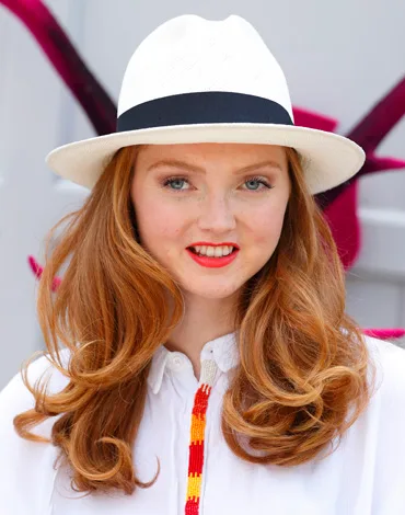 Red-haired woman in a white hat and blouse, smiling at the camera.