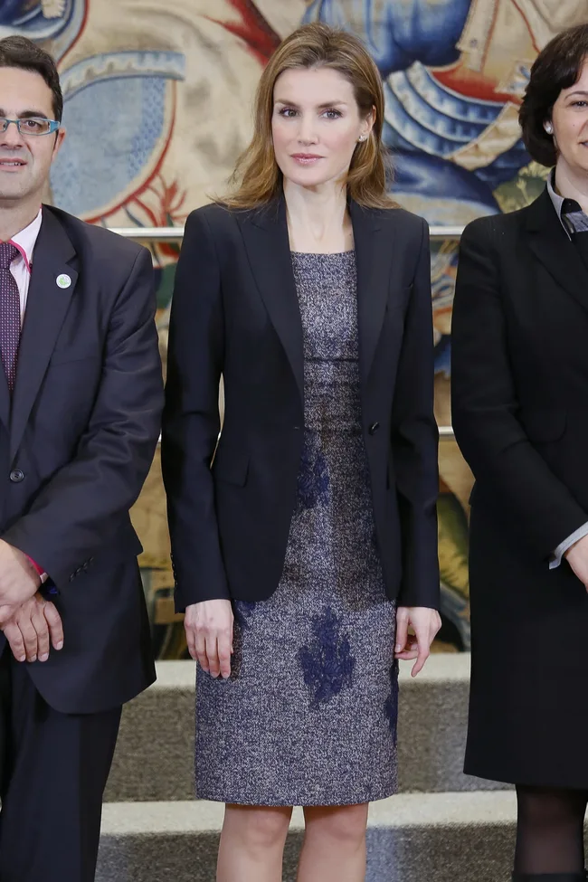 Woman in a navy blazer and patterned dress standing with two others in formal attire.