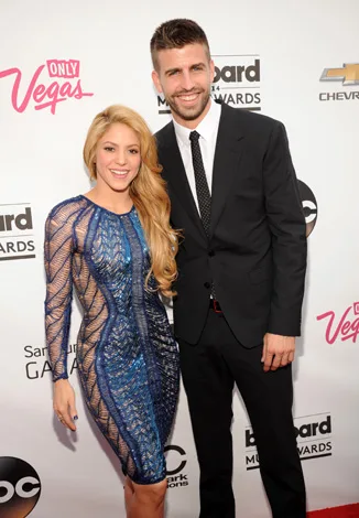 Two people posing on the red carpet; the woman in a blue dress, the man in a suit, against a backdrop with logos.