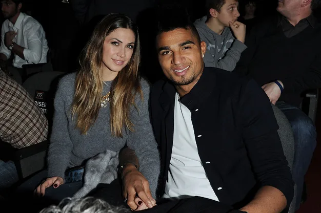 A couple seated together, smiling at an indoor event with people in the background.