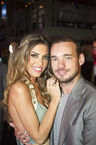 A smiling couple posing closely at a social event, with the woman wearing a beige dress and the man in a gray suit jacket.