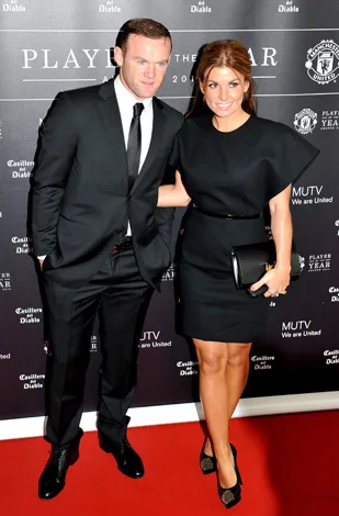 Man in suit and woman in black dress pose on red carpet at Manchester United Player of the Year event.