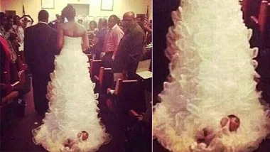 Bride walking down aisle with baby attached to wedding dress train.