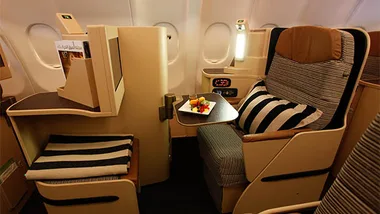 Etihad Airways new business class seat with striped pillow and fruit platter on tray table.