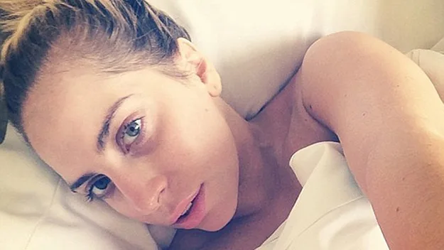 Singer Lady Gaga is lying in bed, makeup-free, looking at the camera with soft lighting.