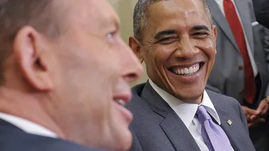 Two men in suits smiling and conversing with each other at a meeting.