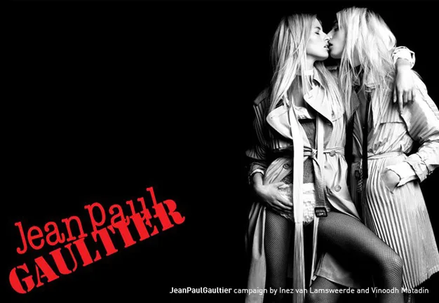 Two models in trench coats pose closely, with Jean Paul Gaultier logo in red on a black background.