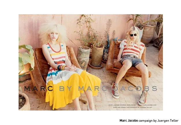 Two models in colorful striped outfits seated outdoors for Marc by Marc Jacobs campaign by Juergen Teller.