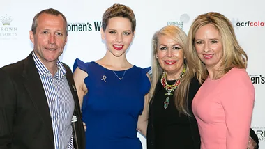 Group of four people smiling at an ovarian cancer awareness event, with women's cancer foundation logos in the background.