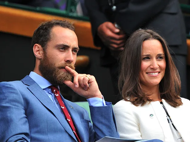 A man in a blue suit sits next to a smiling woman in white attire, both appearing attentive at an event.