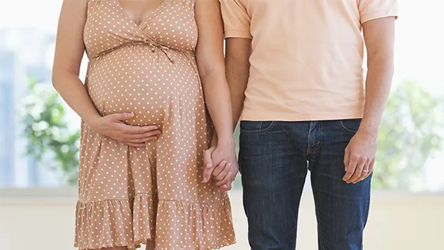 Pregnant woman in polka dot dress holding hands with a man, both standing in a bright room.
