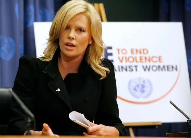 A person speaking at a podium with a sign behind them reading "End Violence Against Women."