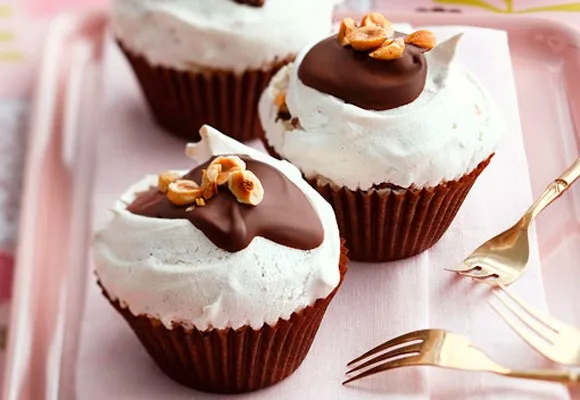 Chocolate cupcakes with whipped topping and nuts on a pink tray beside two golden forks.