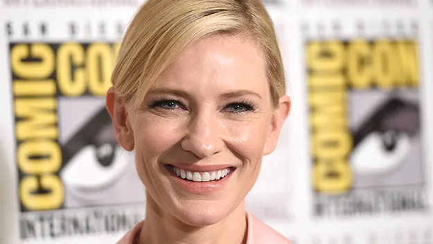 Cate Blanchett smiling at Comic-Con event with banner in the background.
