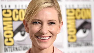 Cate Blanchett smiling at Comic-Con event with banner in the background.