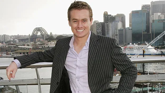 Man in suit smiling in front of Sydney skyline with the Harbour Bridge in the background.