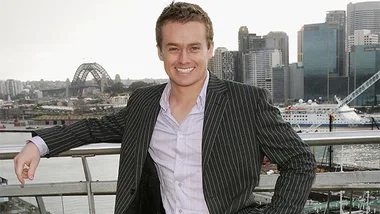 Man in suit smiling in front of Sydney skyline with the Harbour Bridge in the background.