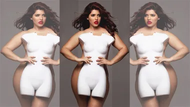 A woman poses confidently in a fitted white outfit with cut-out detailing, showcasing her curves and red lipstick.
