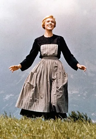 A woman in a dress stands on grass with arms outstretched, set against a cloudy sky backdrop.