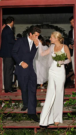Bride in a white gown and groom in a dark suit sharing a moment on a porch during a wedding ceremony.
