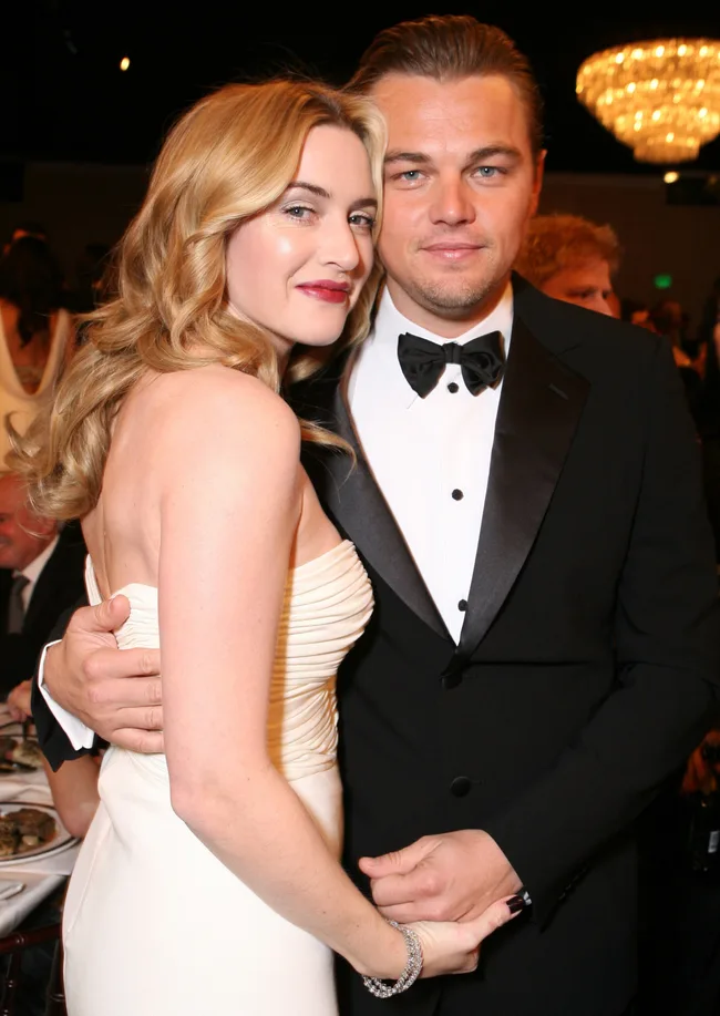A man in a tuxedo and a woman in a white dress pose together at a formal event.
