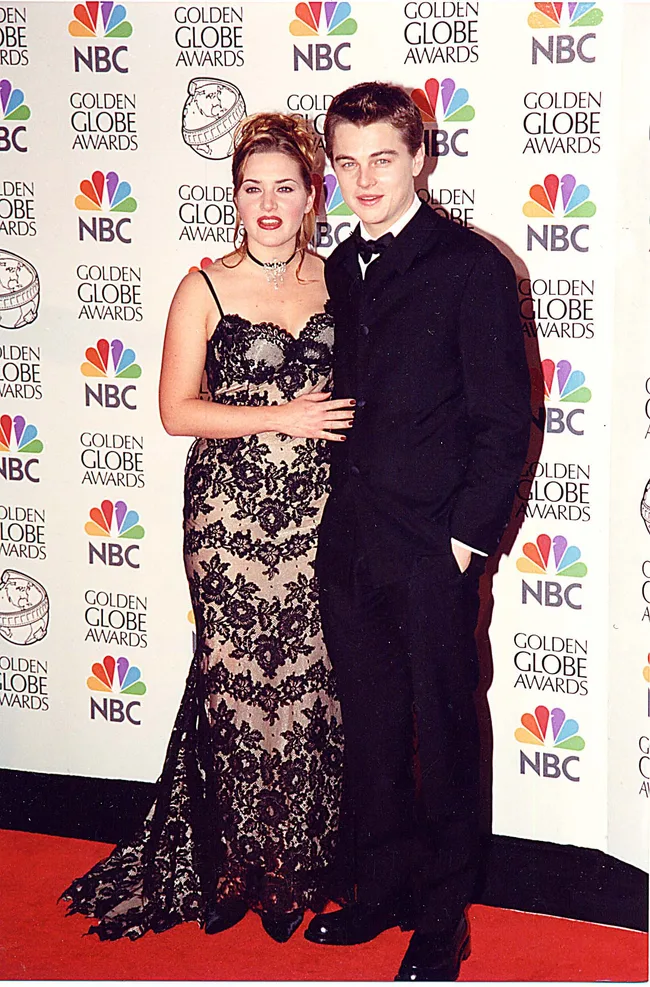 Two people in evening attire on the red carpet at a Golden Globe Awards event, standing in front of a branded backdrop.