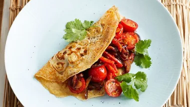 Savory crepe stuffed with cherry tomatoes, onions, and herbs on a white plate garnished with cilantro leaves.