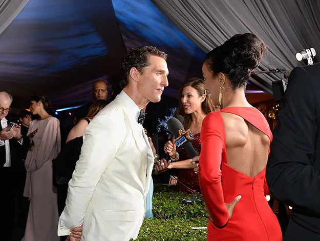 Two people in formal attire engaging in conversation at a glamorous event, surrounded by other guests.
