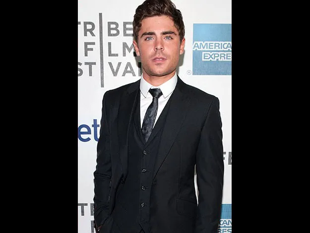 Man in a suit at a film festival event, posing in front of a branded backdrop.