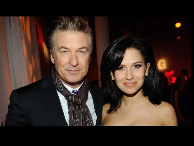 A man in a suit with a scarf and a woman in a strapless dress pose together at an event.