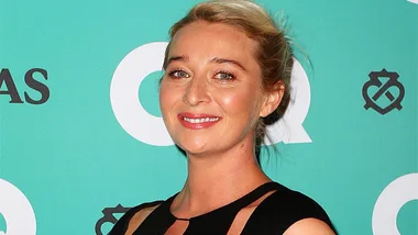 Smiling woman in a black dress at a GQ event with a green background.