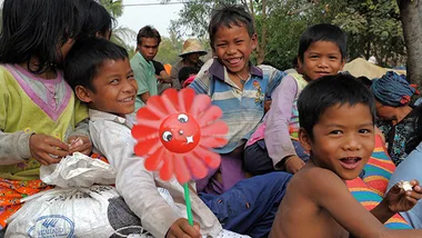 Children smiling and playing with a red flower toy in an outdoor setting.