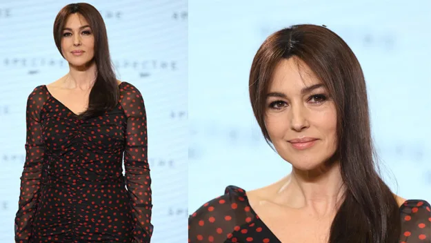 Monica Bellucci at "Spectre" event, wearing black dress with red polka dots, smiling with long brown hair.