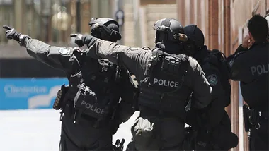 Police in tactical gear pointing and preparing to enter a building during Sydney siege lockdown.