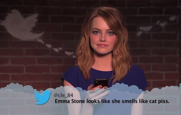 Emma Stone holding a phone and reading a mean tweet about herself on a TV show with a Twitter bird logo in the background.