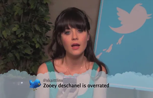 A person reads a mean tweet about "Zooey Deschanel is overrated" with a Twitter bird logo in the background.