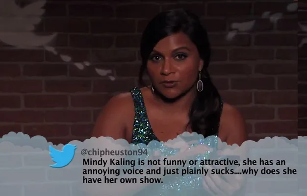 Mindy Kaling reads a mean tweet about herself on a TV show set against a dark brick background.