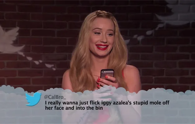 Woman smiling while holding a phone, reading a mean tweet about her appearance on a show.